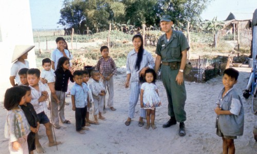 The young lady with the long black hair, is a senior in high school at Danang. Her brother in the checkered shirt on her right accompanies her as she acts as an interpreter between the dental officer and the Vietnamese people as he makes his rounds of the camps and villages.