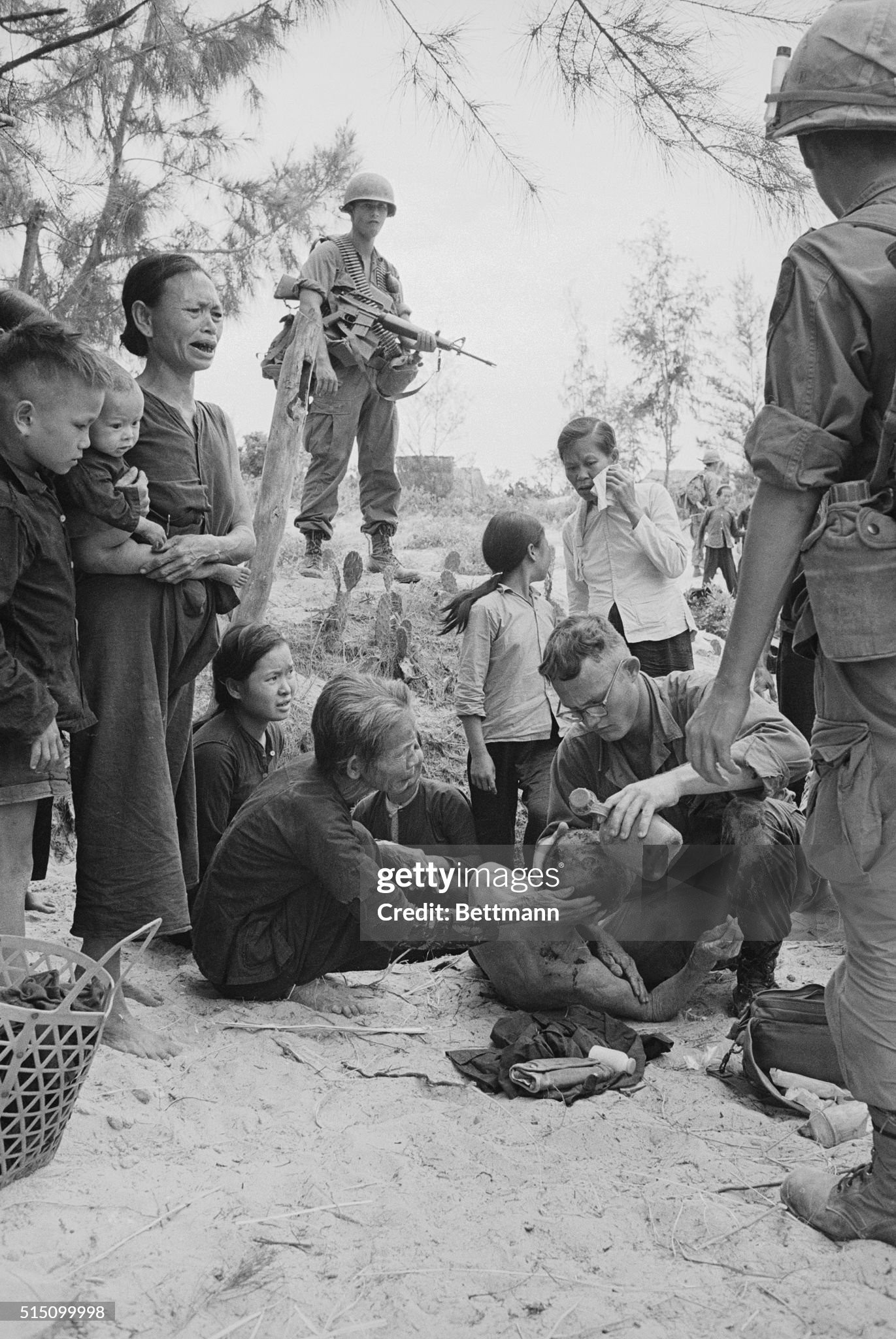 Aids Wounded. Da Nang, S. Vietnam: Trooper of U.S. 1st Cavalry stands guard as he and villagers watch medic treat wounded Vietnamese following brief fighting with enemy forces, near here, during which the small hamlet was razed. The GI's were on a search and destroy mission in the area.