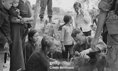 Aids Wounded. Da Nang, S. Vietnam: Trooper of U.S. 1st Cavalry stands guard as he and villagers watch medic treat wounded Vietnamese following brief fighting with enemy forces, near here, during which the small hamlet was razed. The GI's were on a search and destroy mission in the area.