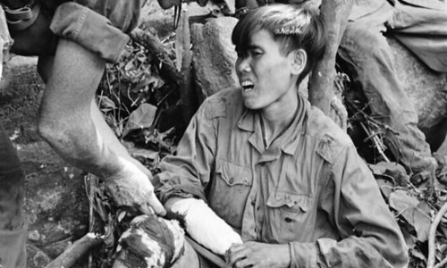 Medical Spec. 4 Roy L. Johnson of Houston, Texas, treats the bloodied knee and arm of one of a group of captured North Vietnamese soldiers on a rocky cliff near Dong Tre, 225 miles northeast of Saigon, in June 1966