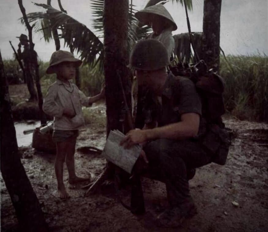Đại úy Donald T. Elledge, Cố vấn Hoa Kỳ của một tiểu đoàn bộ binh QLVNCH,trong chiến dịch hành quân tại Long An , dừng chân hỏi thăm một em bé Việt Nam.