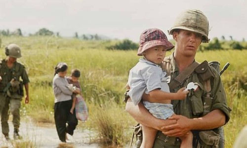 Một người lính Mỹ dù đang hành quân rất vất vả nhưng vẫn sẵn lòng bế theo một em bé Nam Việt Nam.