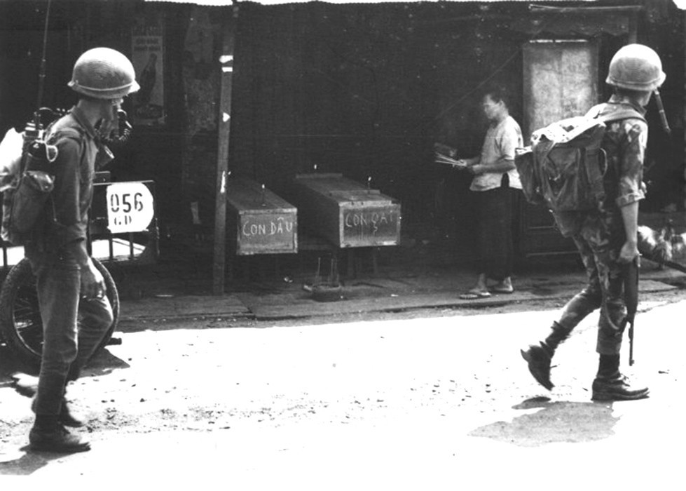Vietnamese soldiers trudge past a grieving mother praying for daughter and daughter-in-law in their coffins Feb 1968 - Photo by Douglas Pike Collection