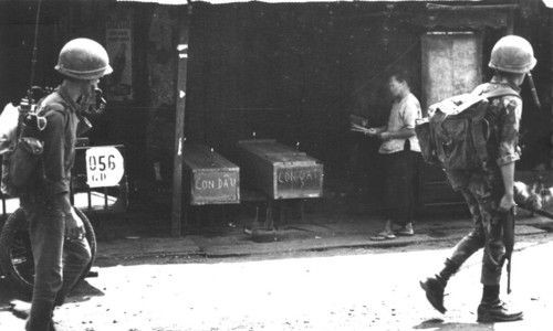 Vietnamese soldiers trudge past a grieving mother praying for daughter and daughter-in-law in their coffins Feb 1968 - Photo by Douglas Pike Collection
